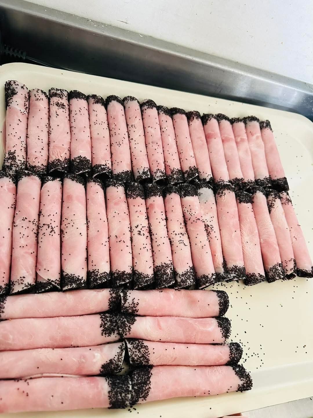 Rolled ham sprinkled with poppy seeds arranged on a serving tray